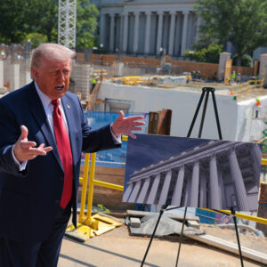 A red-faced President Donald Trump wearing a blue suit and red tie stands next to an easel with an image of his proposed White House ballroom. The backdrop includes the ballroom construction site with workers wearing yellow safety vests.