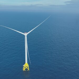 A white wind turbine with three blades each measuring 108 meters long stands against the backdrop of blue ocean waters stretching toward low-hanging clouds on the horizon.