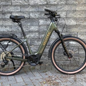 Image of a bicycle with a green, U-shaped frame, leaned up against a grey stone wall.
