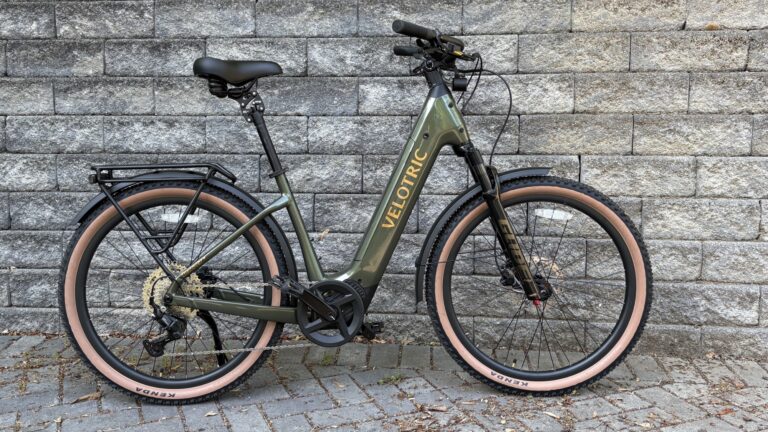 Image of a bicycle with a green, U-shaped frame, leaned up against a grey stone wall.