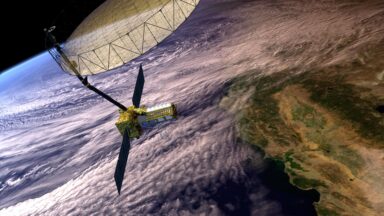 Artist's concept depicts the NASA-ISRO Synthetic Aperture Radar with a main satellite body having two solar panels and a boom attached to the large antenna reflector. The Earth below shows clouds covering the coast of California and the Pacific Ocean.
