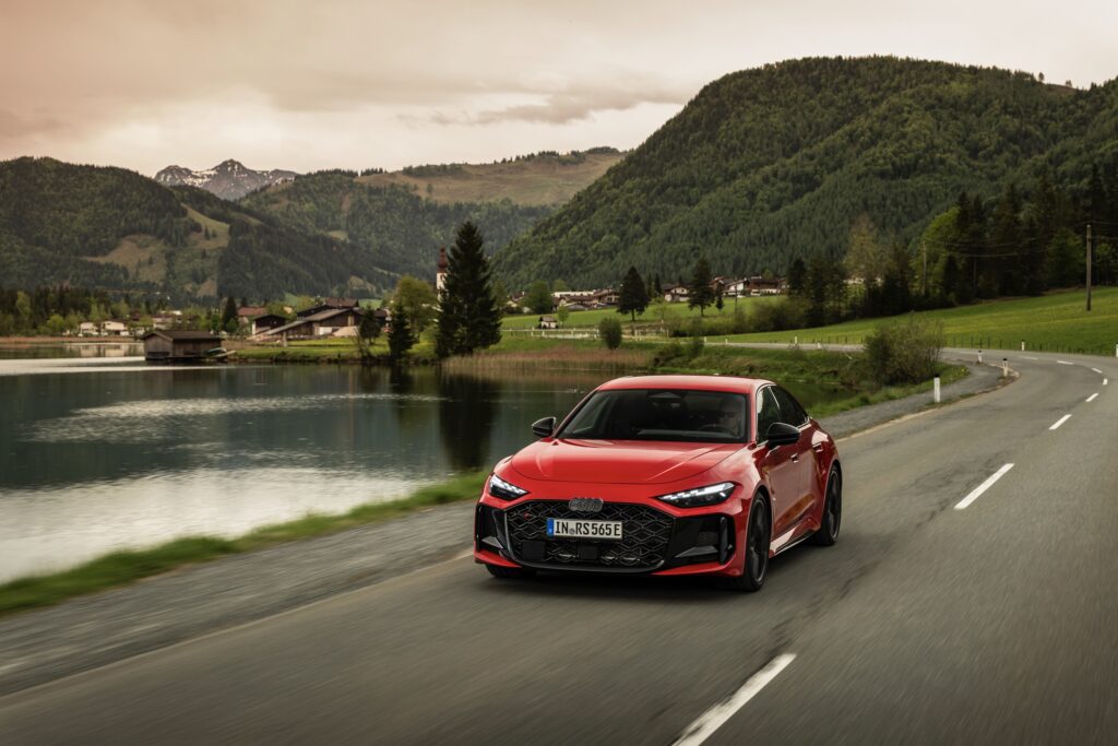 A red Audi RS5 drives past a lake
