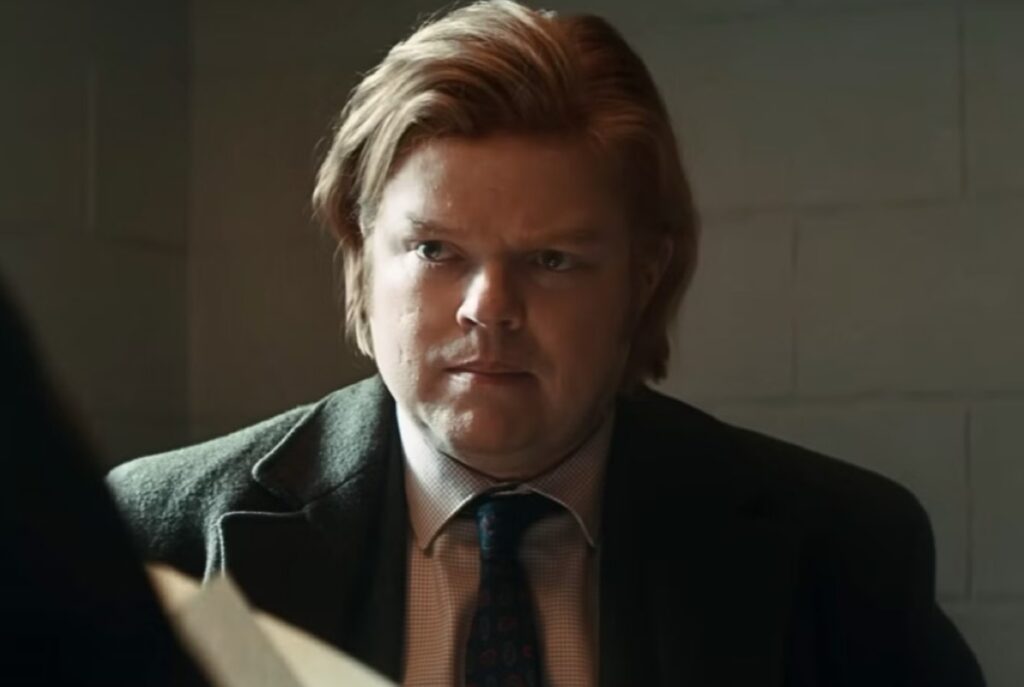 Closeup if young plump man with strawberry blonde hair in a suit, holding papers