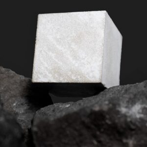 Photo of a small cube of Portland cement resting on pieces of basalt.