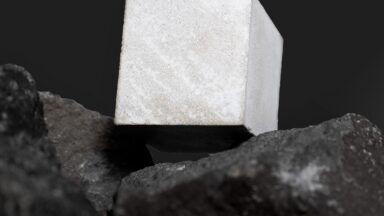 Photo of a small cube of Portland cement resting on pieces of basalt.