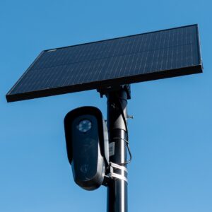 Close-up view of a license plate camera and solar panel mounted on a pole, with the sky in the background.