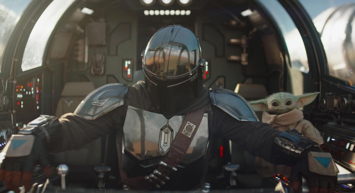 figure in full Mandalorian armor piloting a spaceship with little green figure off to the side