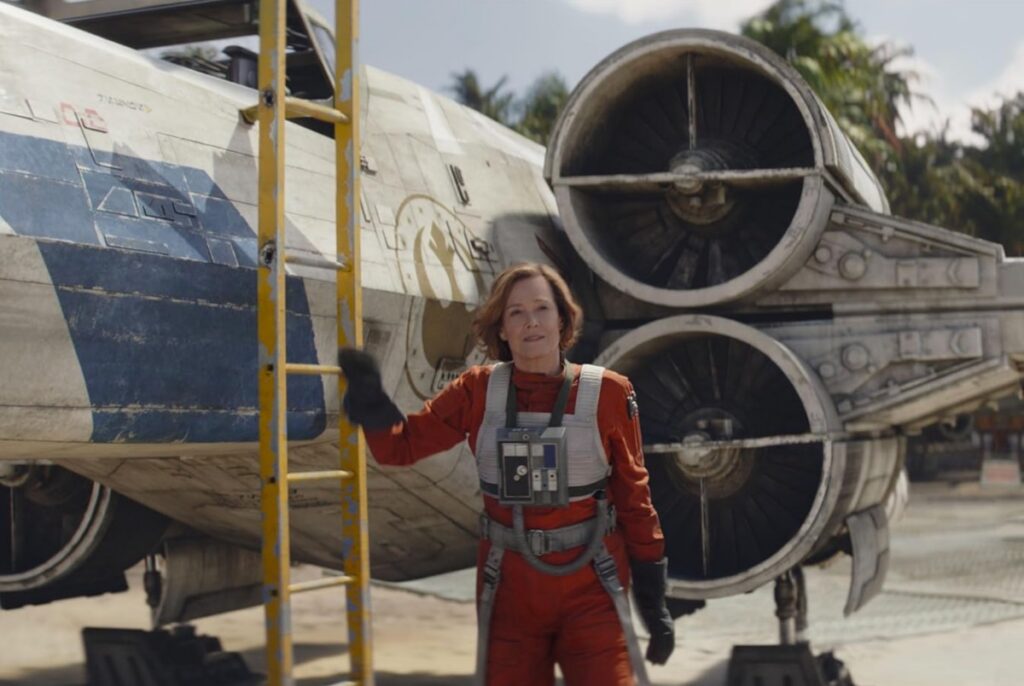 tall woman in red fighter uniform standing next to a fighter spacecraft