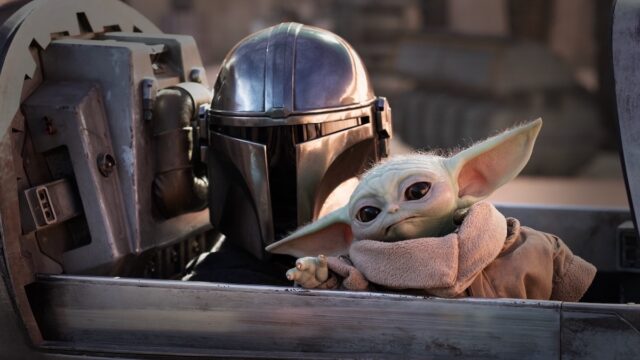 mandolorian in full armor and helmet with little green yoda-like figure sitting in a spacecraft