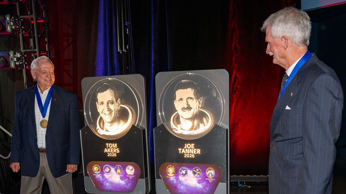 Two men in business suits view etched glass plaques bearing their likeness.