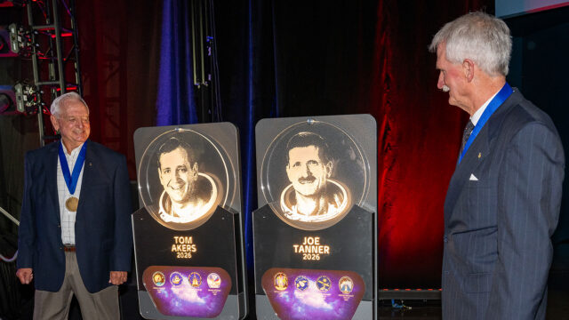 Two men in business suits view etched glass plaques bearing their likeness.