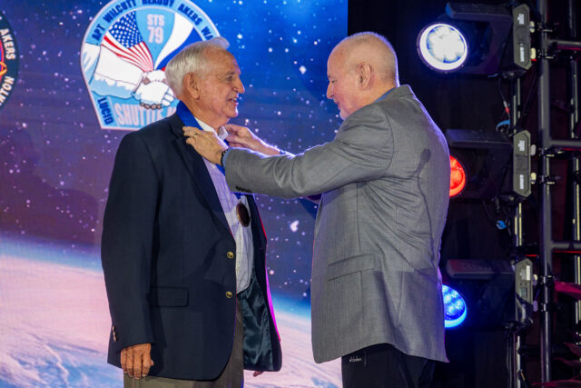 Two men in business suits are pictured one presenting a medal to the other.
