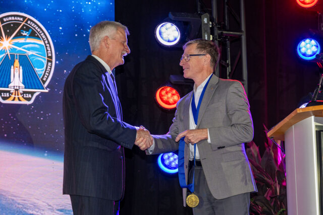 Two men in business suits shaking hands at a ceremony