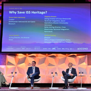 Four people sit on a colorfully-lit stage under a large screen displaying their panel title, names and titles.