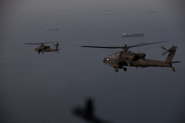 AH-64 Apache helicopters fly above the Strait of Hormuz during a patrol, April 17. Commercial ships are visible on the water below.