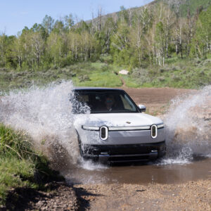 A white Rivian R2 splashes through a stream