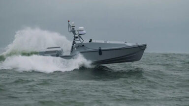 An image of the Corsair autonomous surface vessel developed by Saronic Technologies racing across the surface of a blue-gray ocean with white water foam in its wake.