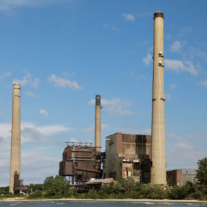 A river with a large power plant with three smokestacks on the shore.
