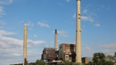 A river with a large power plant with three smokestacks on the shore.