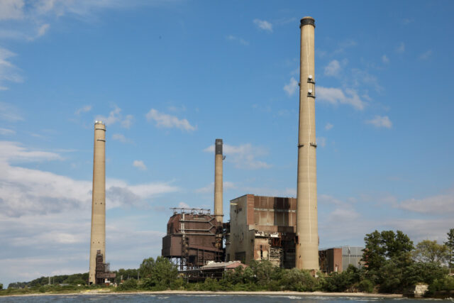 A river with a large power plant with three smokestacks on the shore.