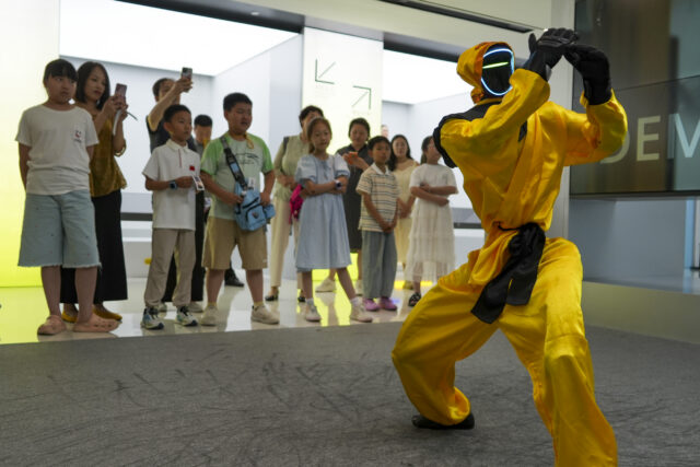 Children watch a martial arts performance by Unitree robots at a humanoid robot store on June 1, 2026 in Zhengzhou, Henan Province of China. The robot is wearing yellow martial arts clothing.