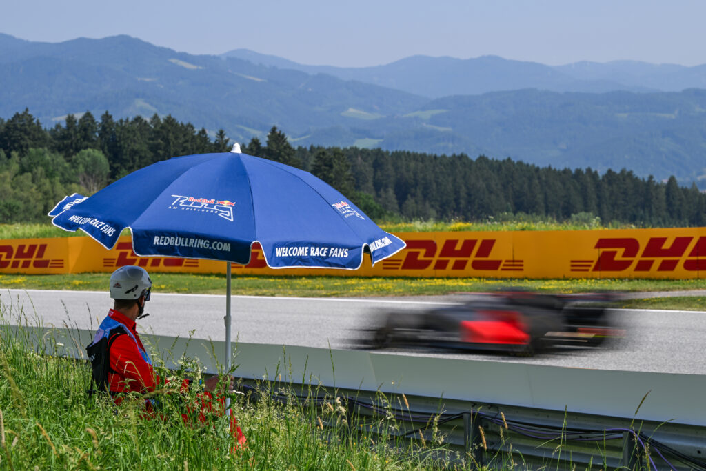 SPIELBERG, AUSTRIA - JUNE 28: A track marshal sits beneath a blue Red Bull Ring umbrella as a car passes in a motion blur during the F1 Grand Prix of Austria at Red Bull Ring on June 28, 2026 in Spielberg, Austria. (Photo by Artur Widak/NurPhoto via Getty Images)