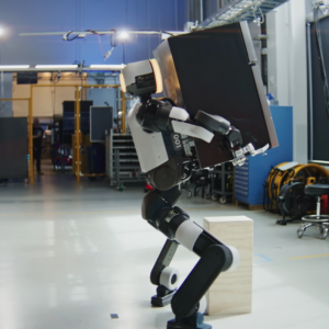 An Atlas humanoid robot developed by Boston Dynamics crouches as it lifts a mini fridge.
