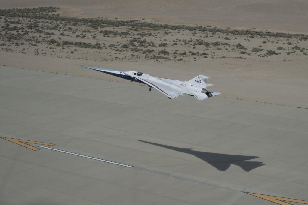 NASA’s X-59 quiet supersonic research aircraft approaches landing at Edwards Air Force Base in California on Thursday, March 26, 2026. The aircraft is seen with landing gear extended and its shadow on the runway below.