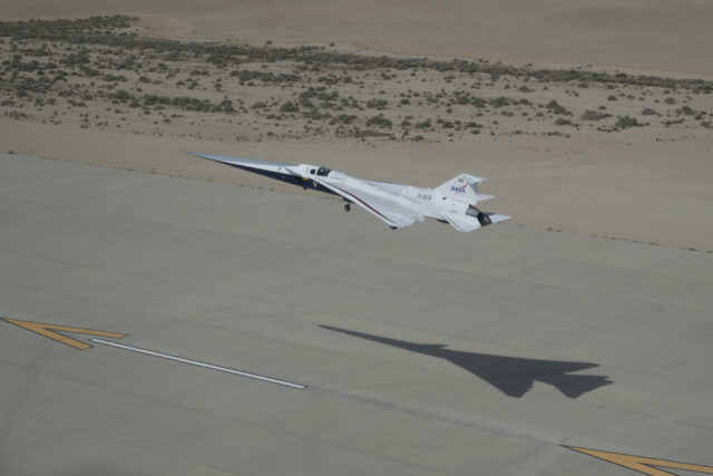 NASA’s X-59 quiet supersonic research aircraft approaches landing at Edwards Air Force Base in California on Thursday, March 26, 2026. The aircraft is seen with landing gear extended and its shadow on the runway below.