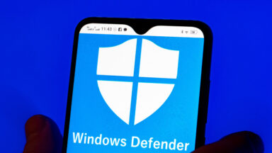 In this photo illustration, the Microsoft Windows Defender logo is seen displayed on a smartphone and Microsoft logo in the background.