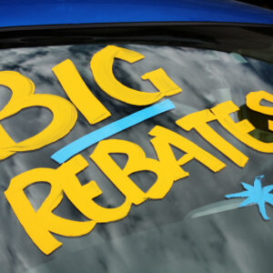 "Big Rebates" written on a new car in a dealership car lot.