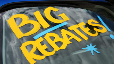 "Big Rebates" written on a new car in a dealership car lot.