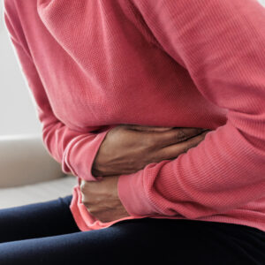 Close-up of unrecognizable black woman sitting on couch holding her abdomen in pain.
