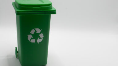 Green recycling bin with the recycling symbol on a white background.