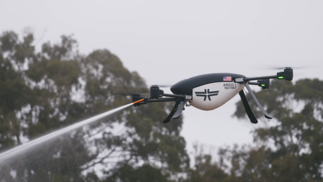 An Argo-1 quadcopter drone developed by Seneca is shown hovering in a side profile while spraying fire suppressant from
