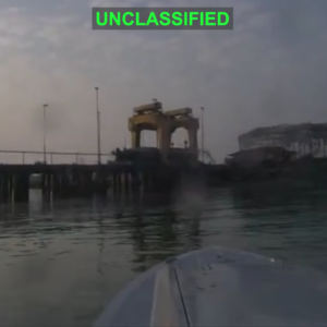 An unclassified video showed a US military explosive drone boat approaching an Iranian naval facility where a midget submarine is suspended from a gantry.
