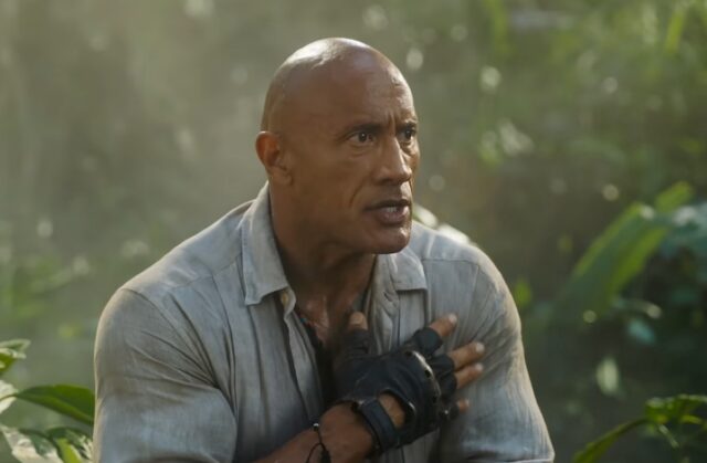 muscular bald man standing looking confused in a jungle