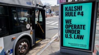 A Kalshi advertisement at a bus stop displays the text, "We operate under US law because Kalshi is a federally regulated US exchange."