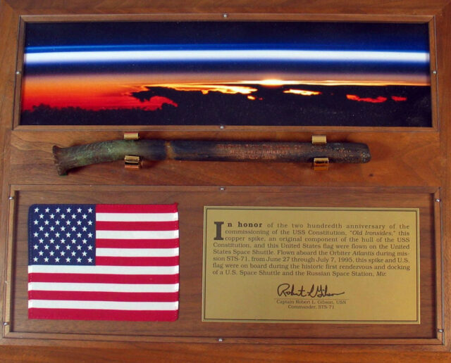 a wooden plaque on which a small American flag, a copper spike and a brass plate have been mounted.