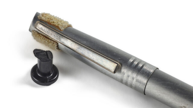 a black plastic piece and a chrome-colored pen with velcro attached to its top