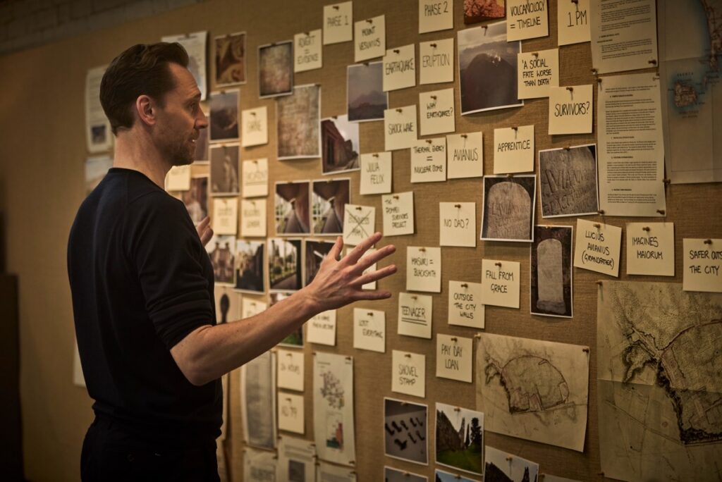 Hiddleston examines a pinboard with clues as to how the events at Pompeii unfolded after the eruption of Mt. Vesuvius.