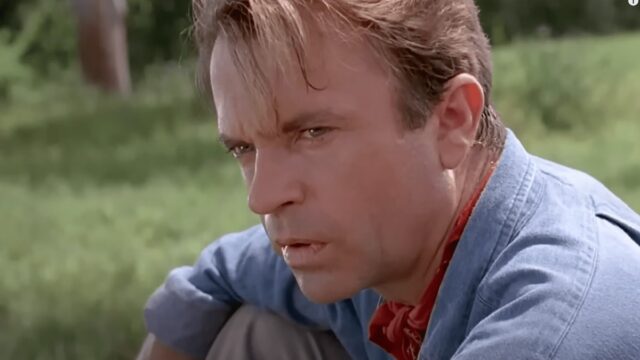 ruggen paleontologist in blue shirt and red kerchief looking intently off to the side while sitting in a jungle clearing