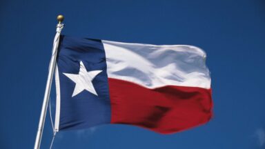A Texas state flag blowing in the wind with the sky in the background