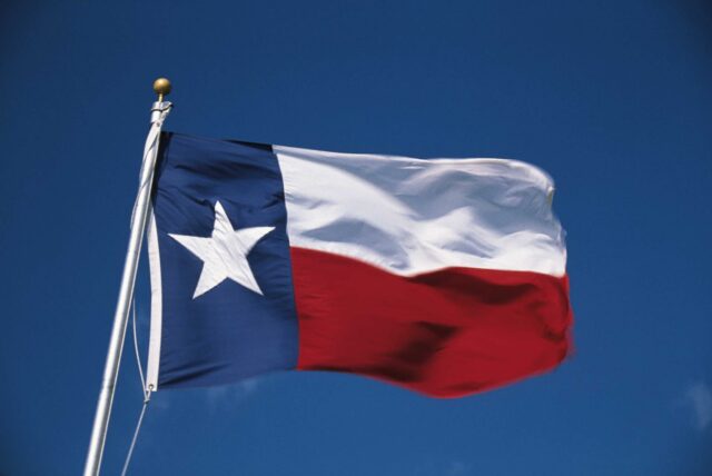 A Texas state flag blowing in the wind with the sky in the background