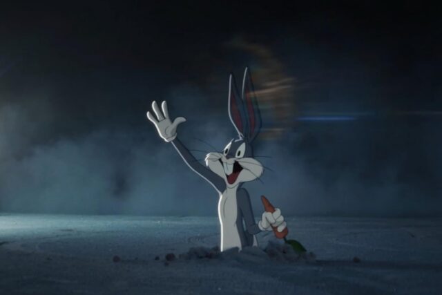 cartoon Bugs Bunny popping out of a hole in the ground holding a carrot and waving with the other hand