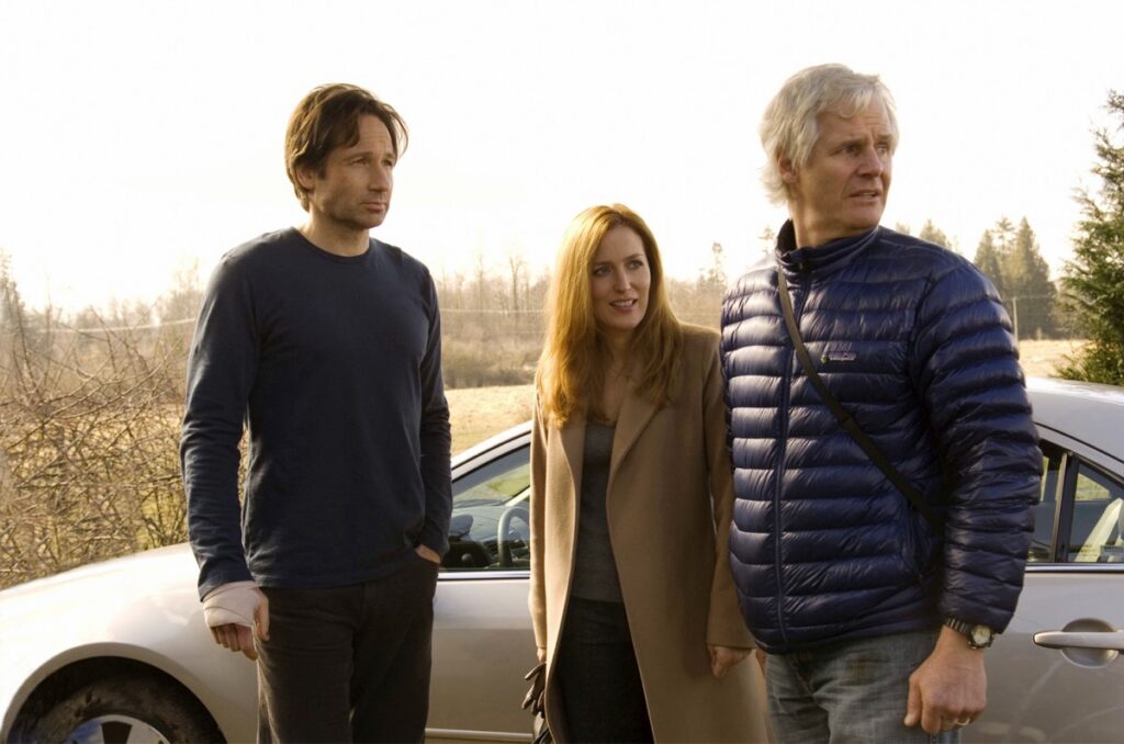 stars David Duchovny and Gillian Anderson standing in front of a car with director Chris Carter