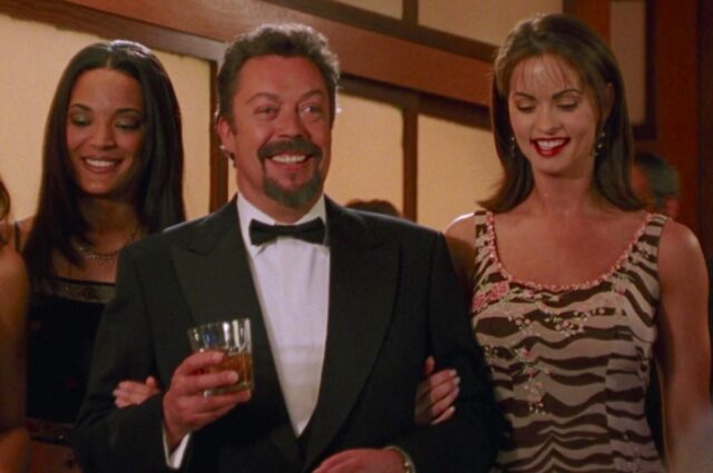 rich man smiling and holding a glass of champagne surrounded by beautiful women