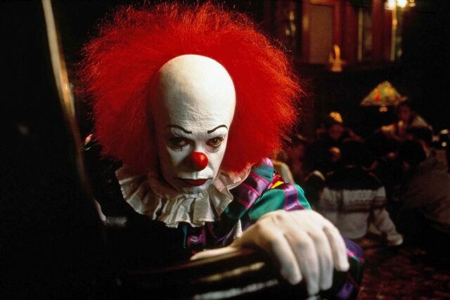 ominous lookin circus clown staring into the camera while seated
