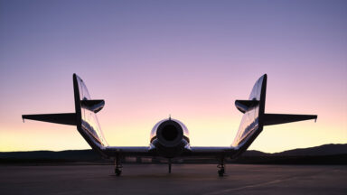 A spaceplane is silhouetted by the sun while sitting outside a hangar