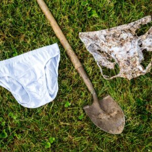 A new pair of cotton underwear, a pair that's partially buried in the ground, and a shovel lying between them in the grass.